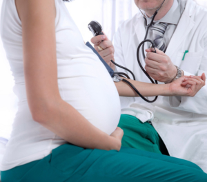 mid-section-of-pregnant-woman-with-doctor-taking-her-blood-pressure