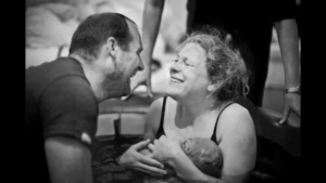 woman-holding-newborn-in-birthing-pool-with-partner