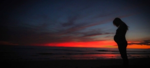 pregnant-woman-standing-on-the-beach-with-sunset-behind-her