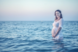 pregnant-woman-standing-in-the-ocean-holding-her-belly