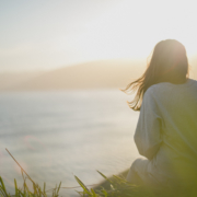 womans-back-sitting-on-cliff-overlooking-the-ocean