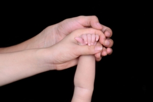 two adult hands holding a baby's hand